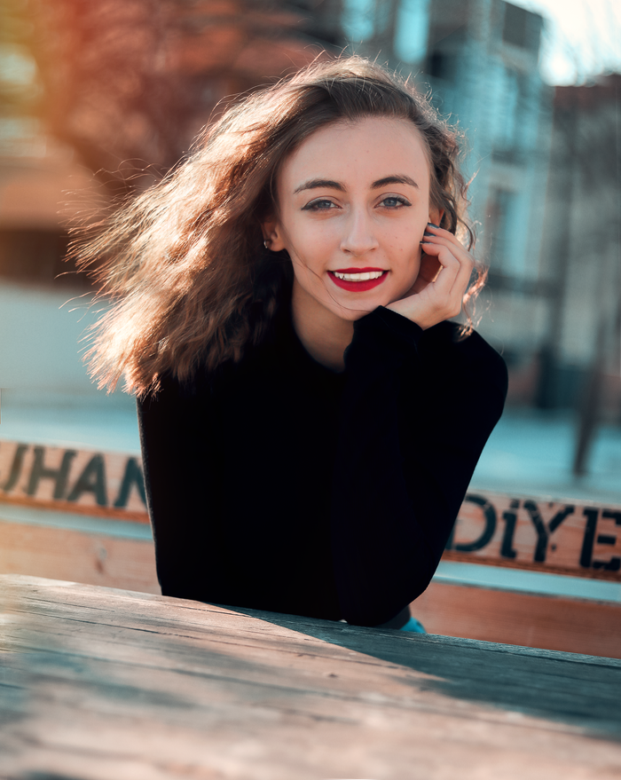 Vibrant portrait of a smiling woman with flowing hair and red lips sitting outdoors on a sunny day.